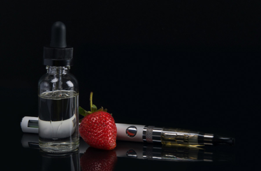 Vape device with e-liquid and a strawberry next to it 900x589