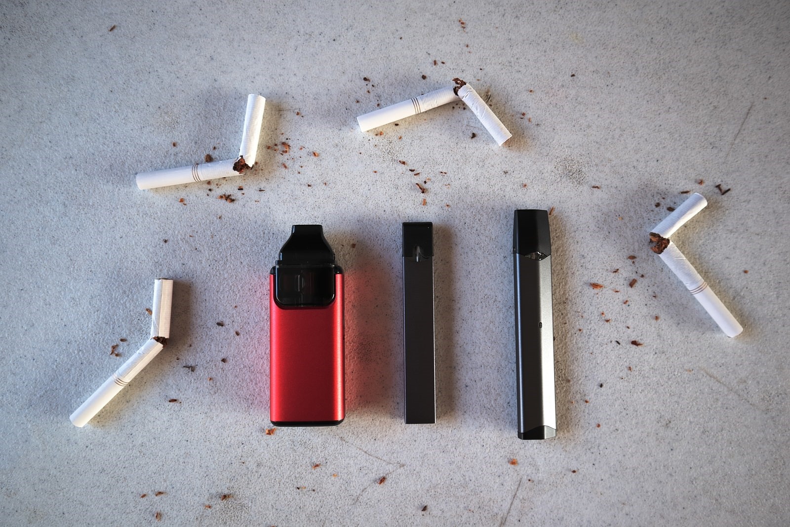 Vape devices surrounded by broken cigarettes