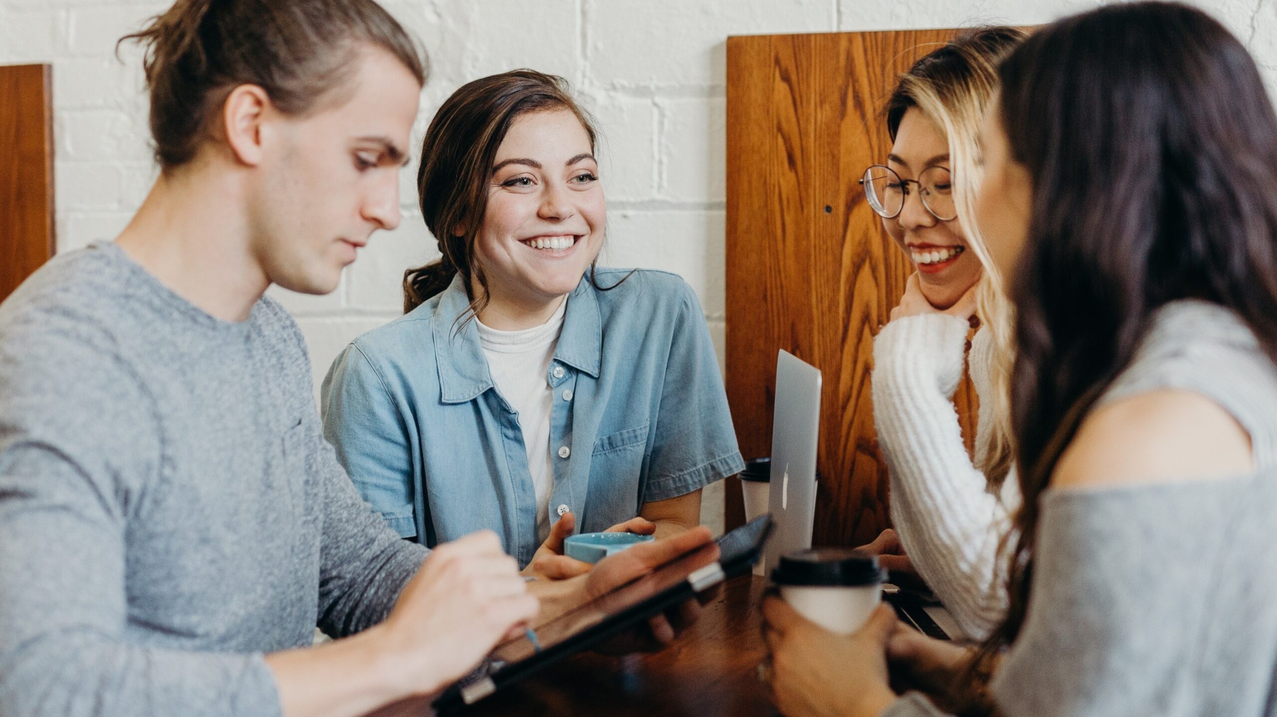 Four people smiling and talking at a table with laptops and coffee.
