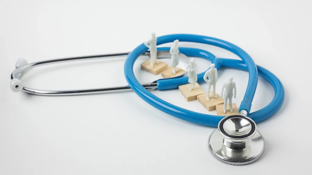 Stethoscope encircling miniature figures on wooden blocks, symbolizing healthcare teamwork.