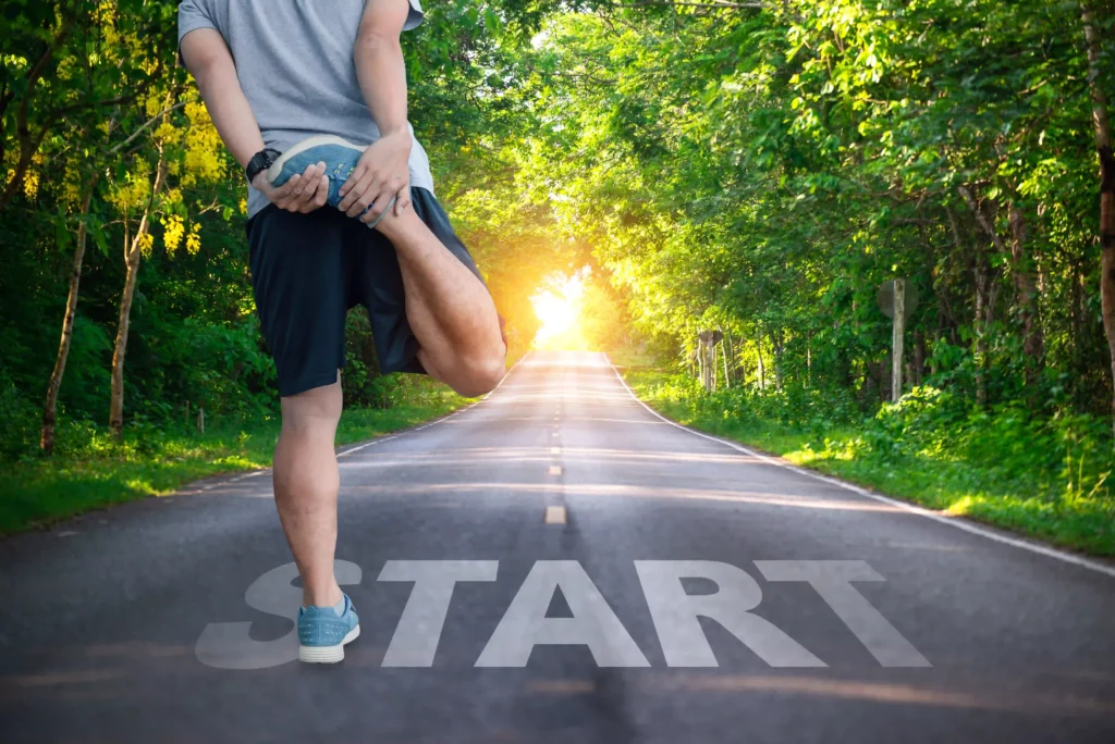 Person stretching on road with "START" painted, surrounded by trees.