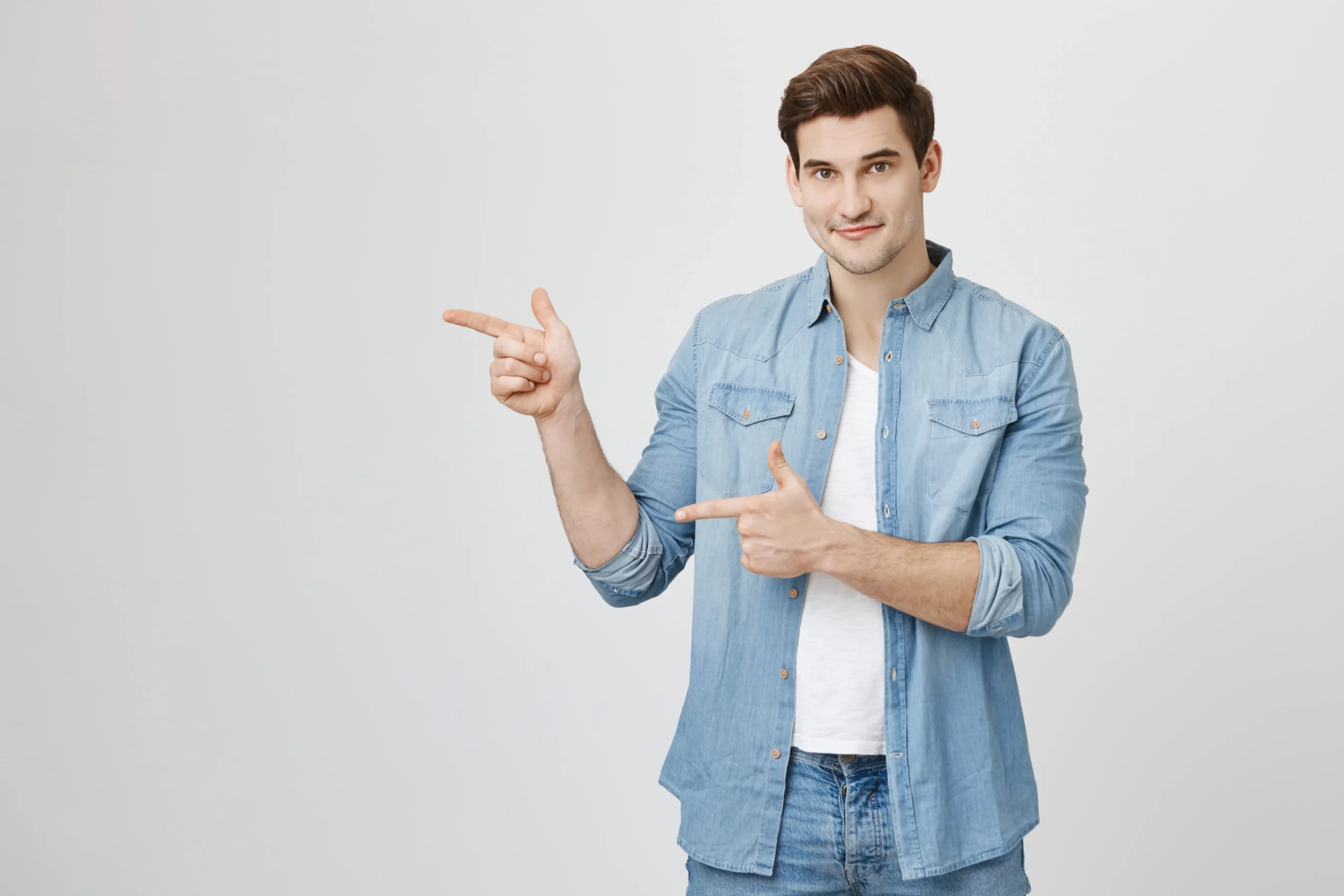 Man in denim shirt pointing sideways with both hands.