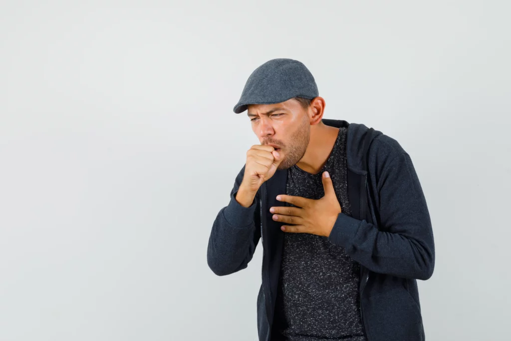 Man in a cap coughing into his hand.