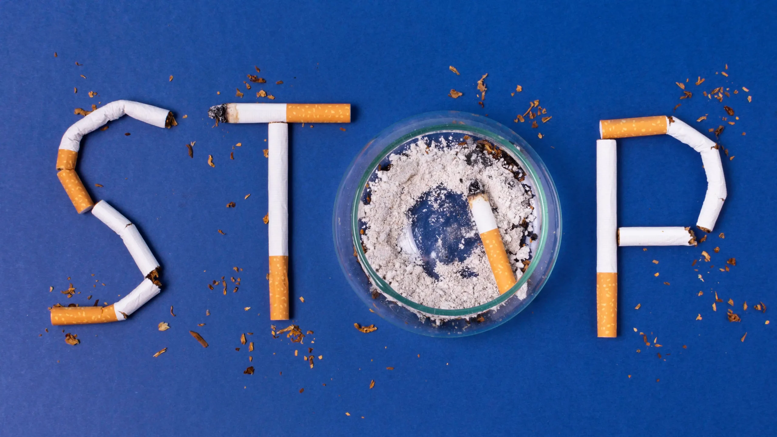 Cigarette butts spelling "STOP" with ashtray on blue background.