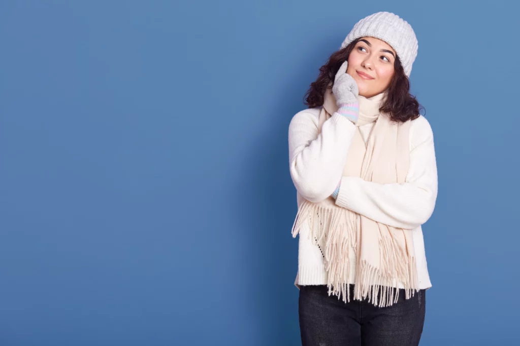 Woman in winter clothing, looking thoughtful against a blue background.