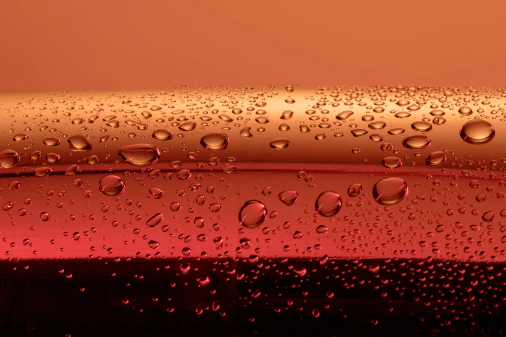 Water droplets on a red reflective surface with an orange background.