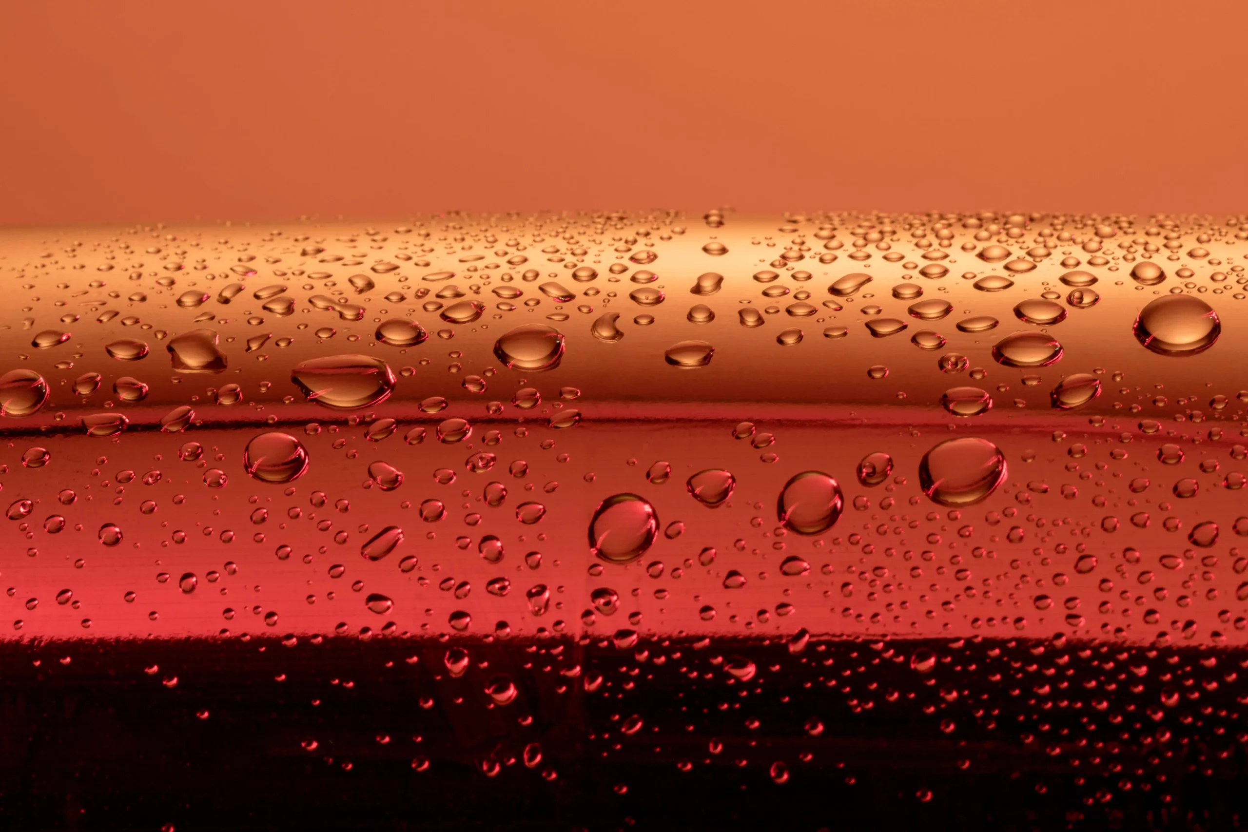 Water droplets on a red reflective surface with an orange background.