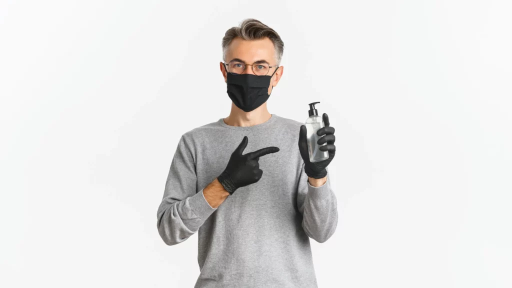 Man in mask and gloves holding hand sanitizer bottle.