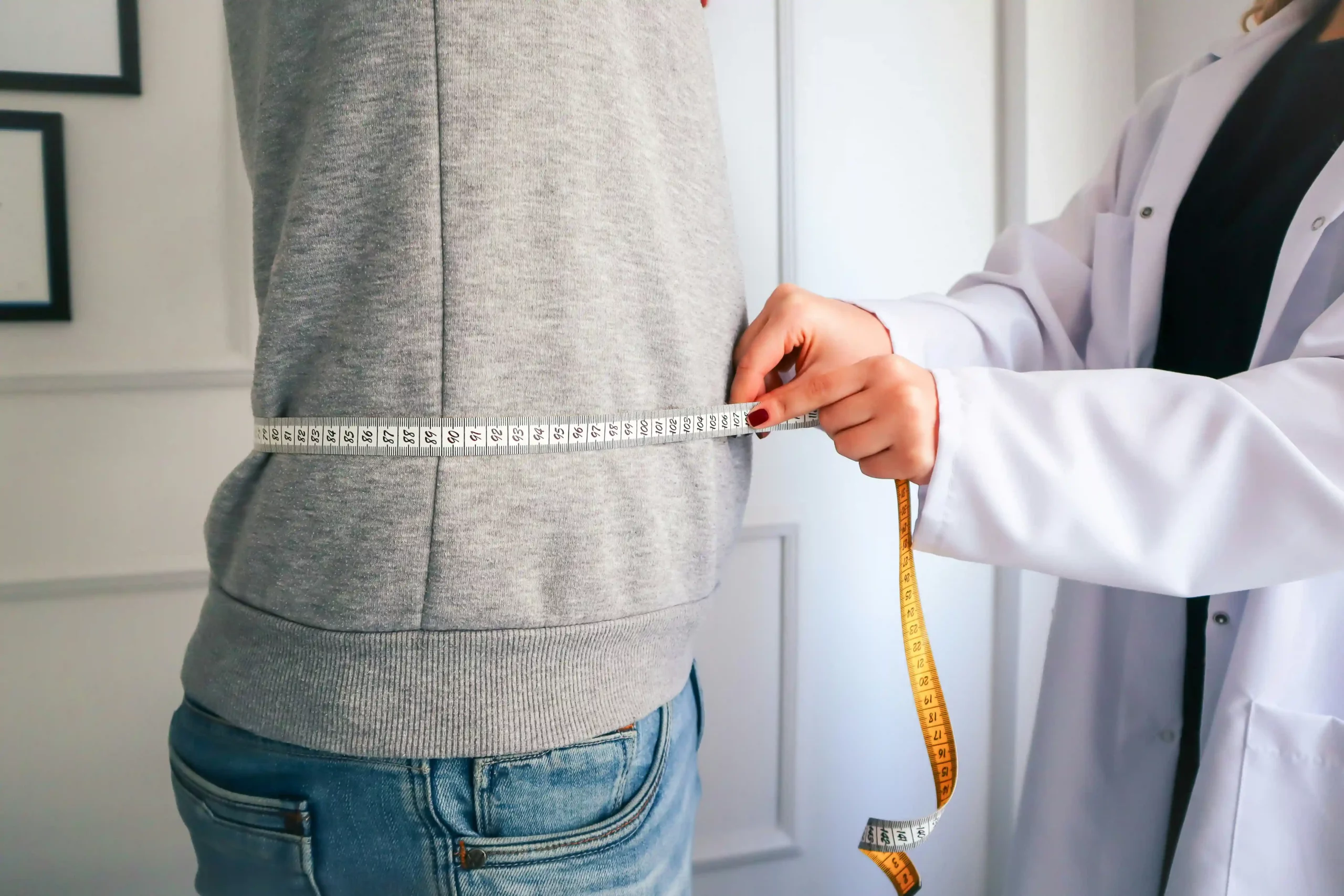 Doctor measuring a person's waist with a tape measure.