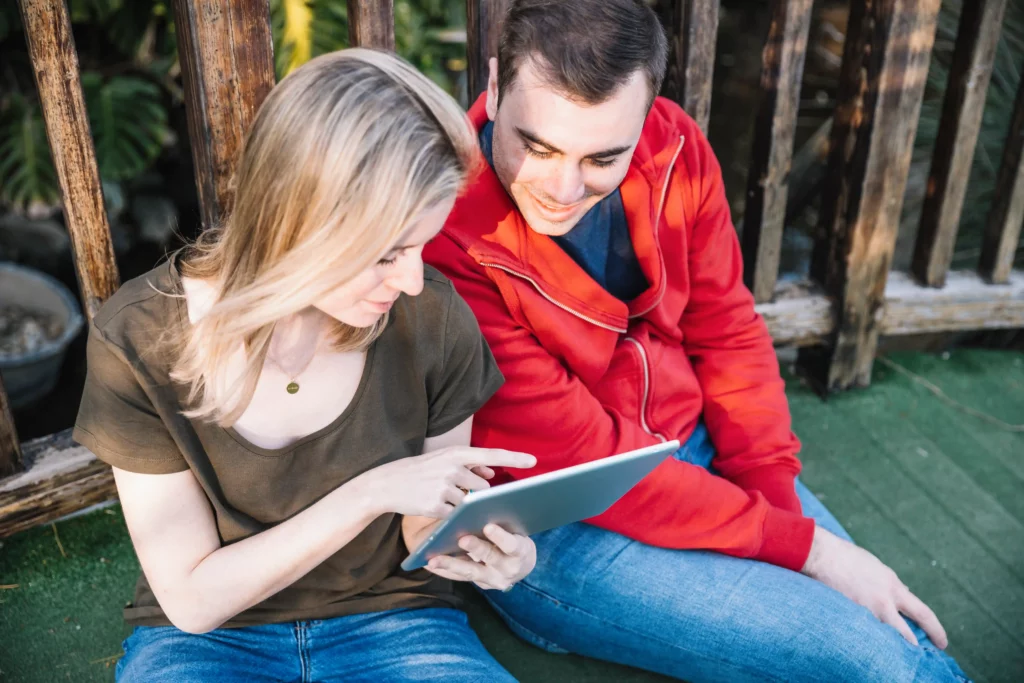 Two people sitting outside, looking at a tablet together.