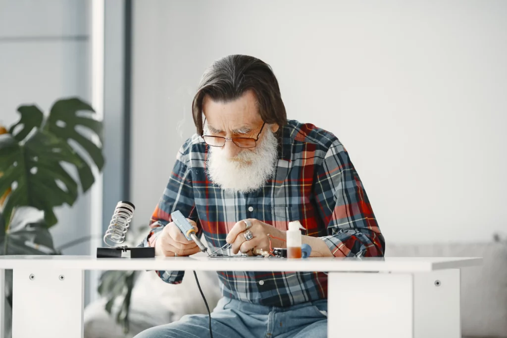Elderly man soldering electronics at a table.
