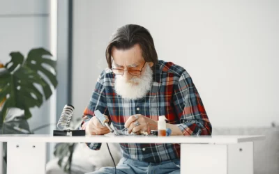 Elderly man soldering electronics at a table.